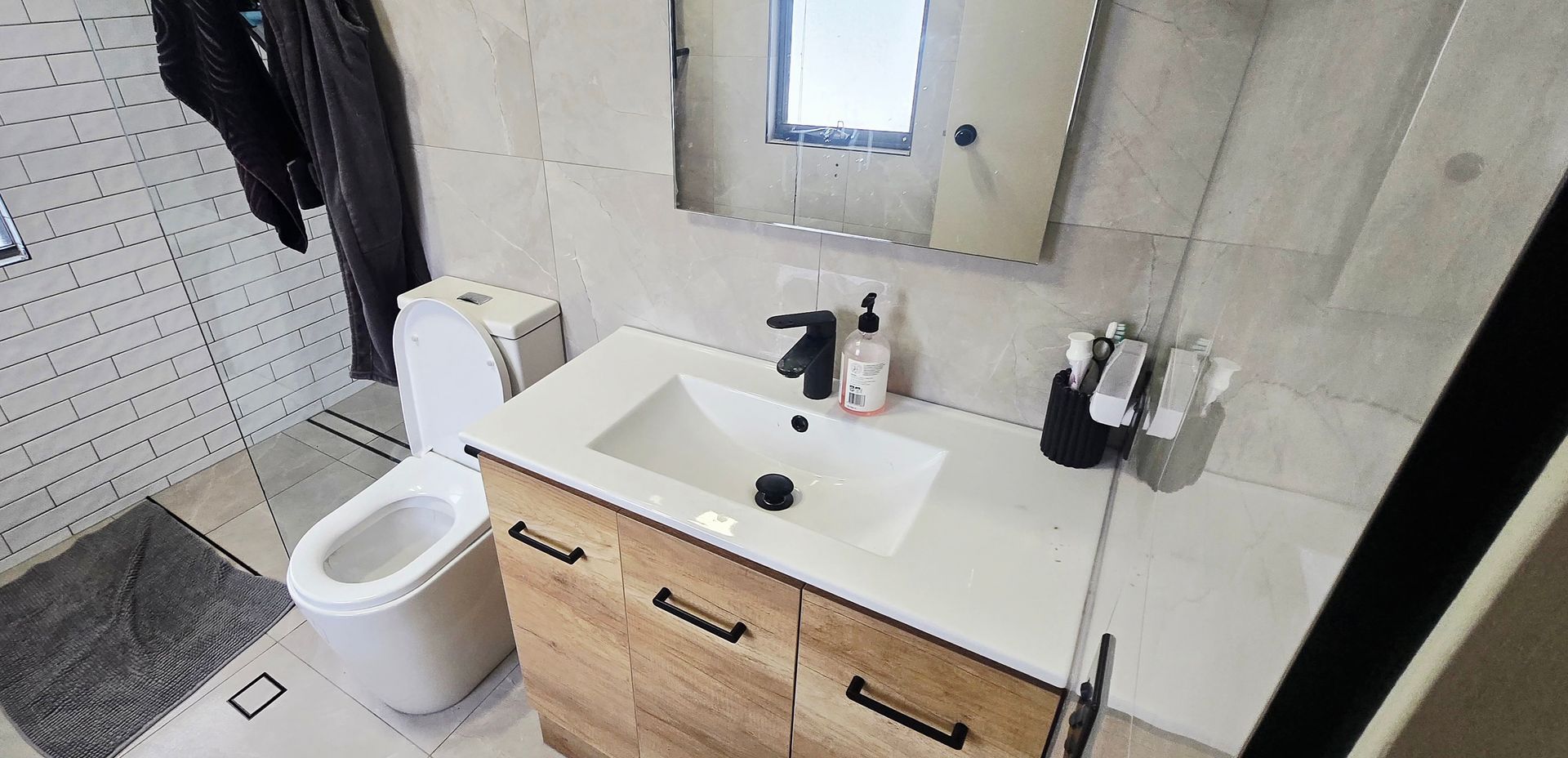 Small modern bathroom with toilet, vanity sink, mirror, and black-and-white tiled walls.