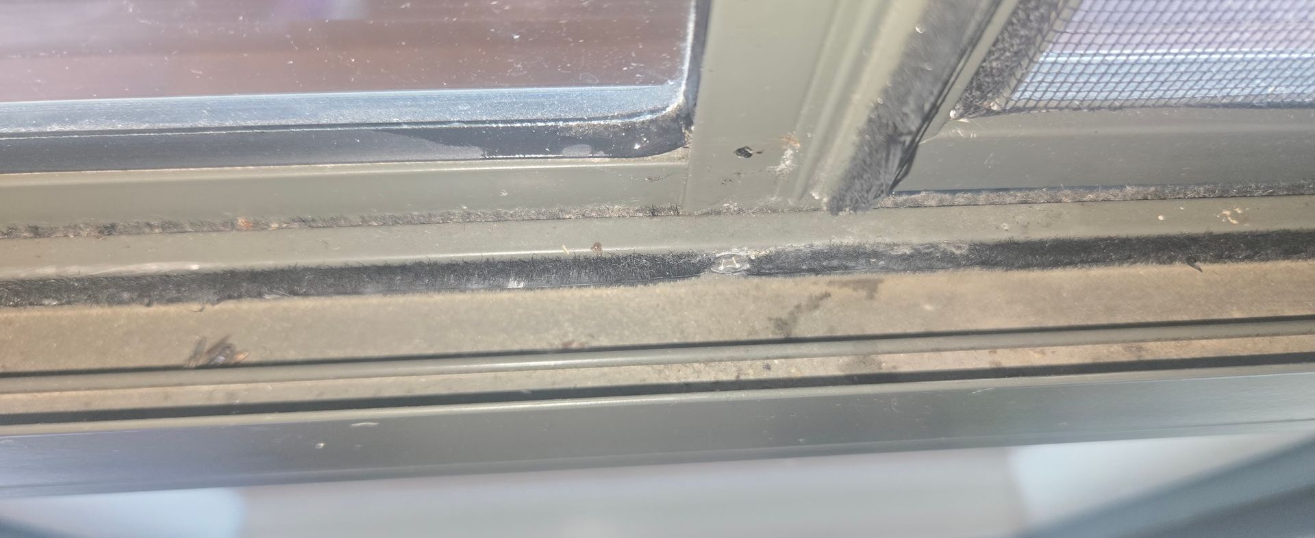 Close-up of a dirty window frame and tracks with metal trim and a blurry view outside