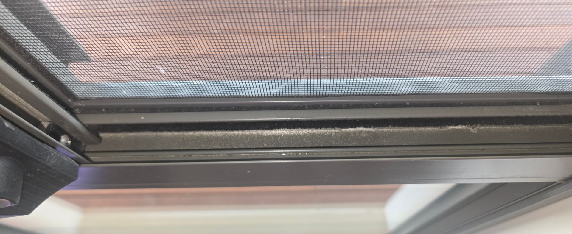 Interior view of cleaned window tracks with dark metal framing and a mesh screen above