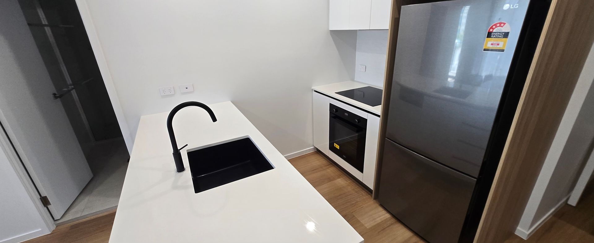 Compact kitchen with white island, black faucet, stove, and stainless steel refrigerator. Furnished clean apartment in Surfers Paradise