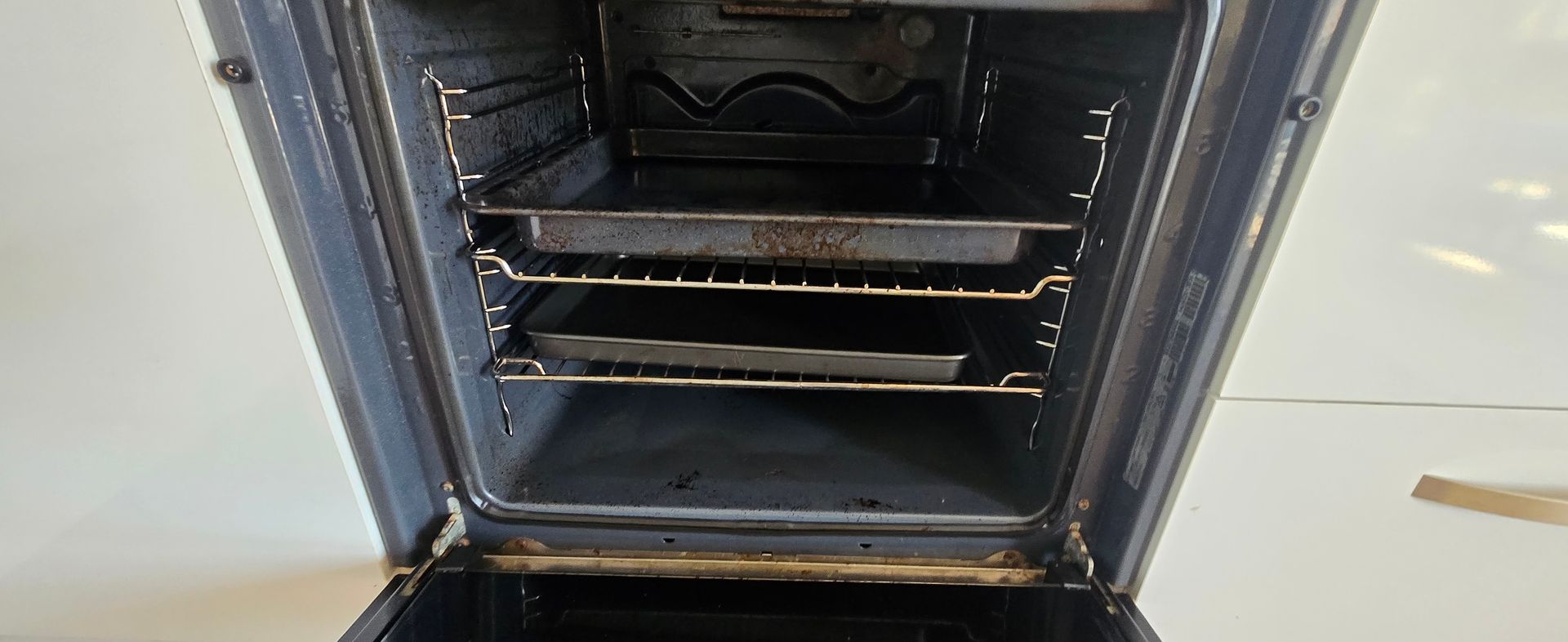 Open dirty black oven with empty metal racks and a dark interior