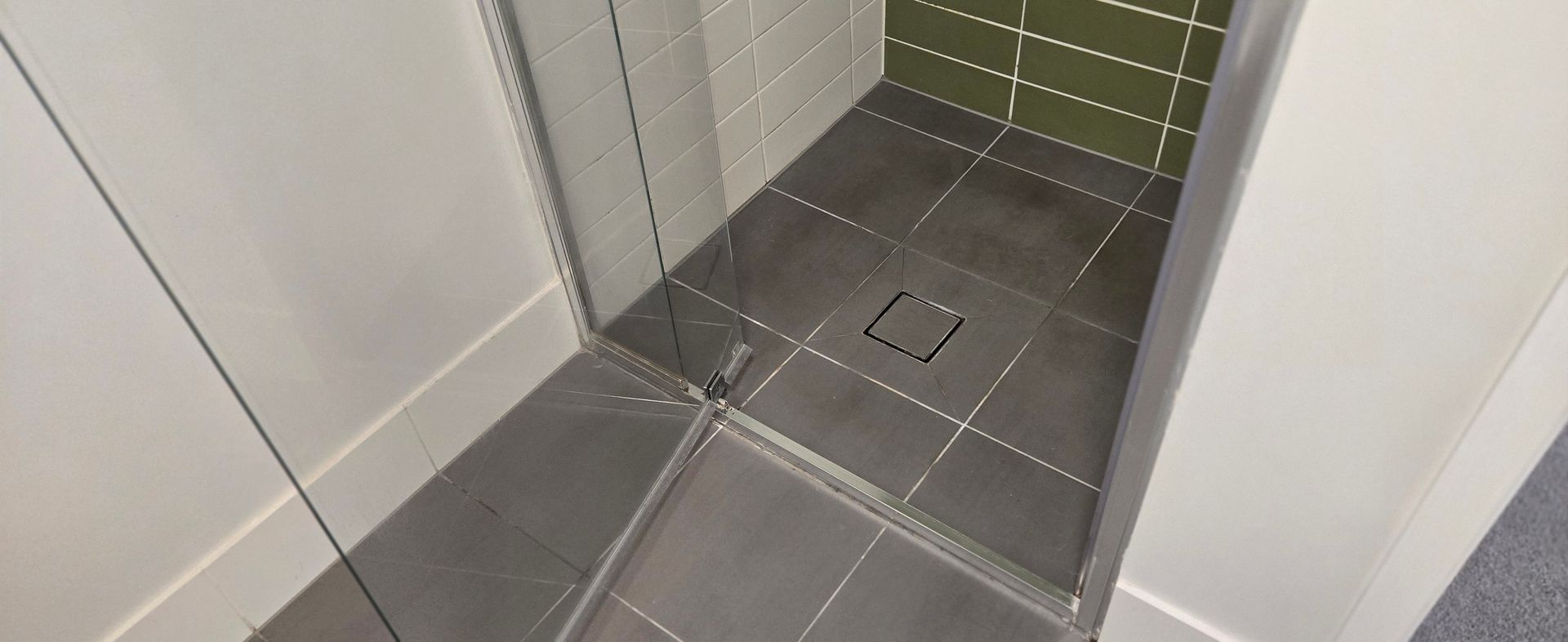Clean, free of mould and free of calcium build up, tiled shower floor with a drain and green mosaic wall tiles