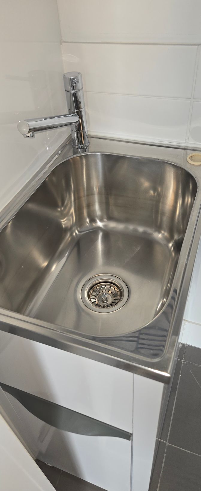 White tiled bathroom floor with a drain hole and tiled walls, viewed from a low angle