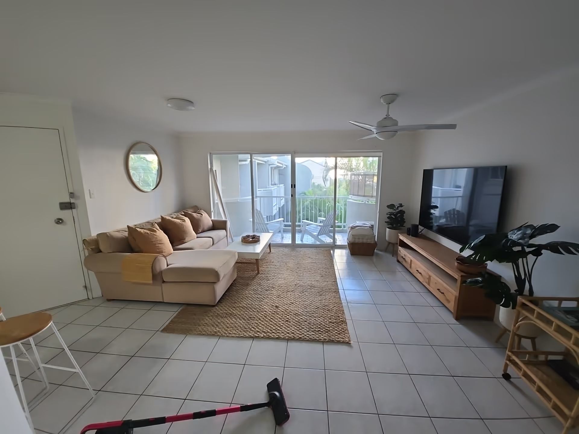 Bright living room with beige sofa, TV, sliding glass doors, and tiled floor. Clean airbnb apartment in Main Beach