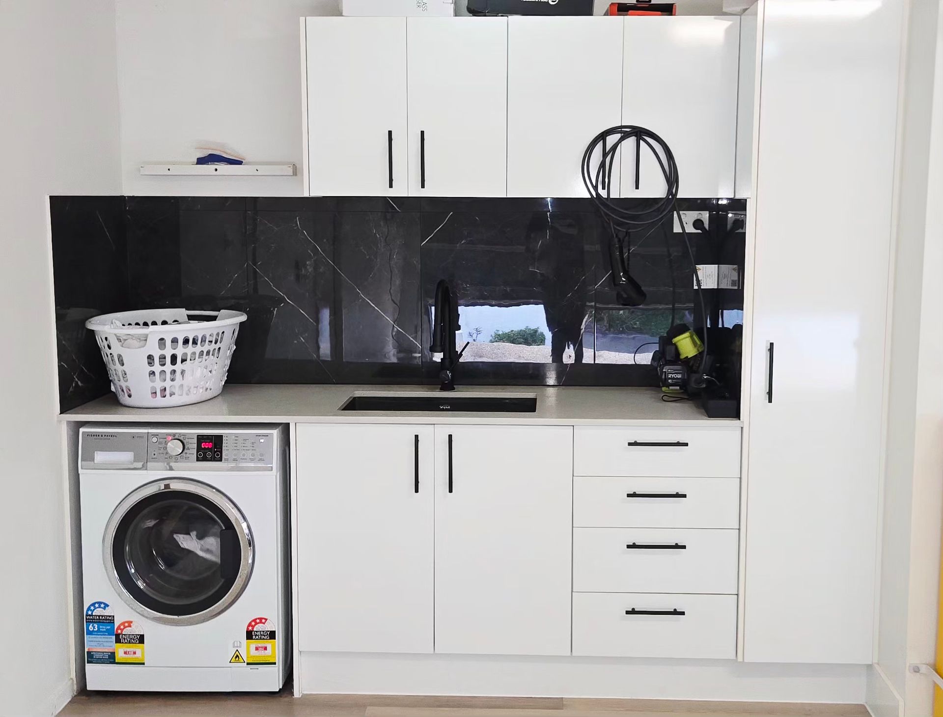 Modern laundry room with white cabinets, black backsplash, washing machine, and sink counter