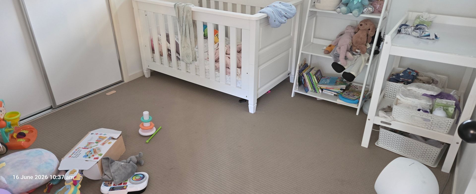 Nursery with a white crib, toy basket, and scattered baby toys on a beige carpet.