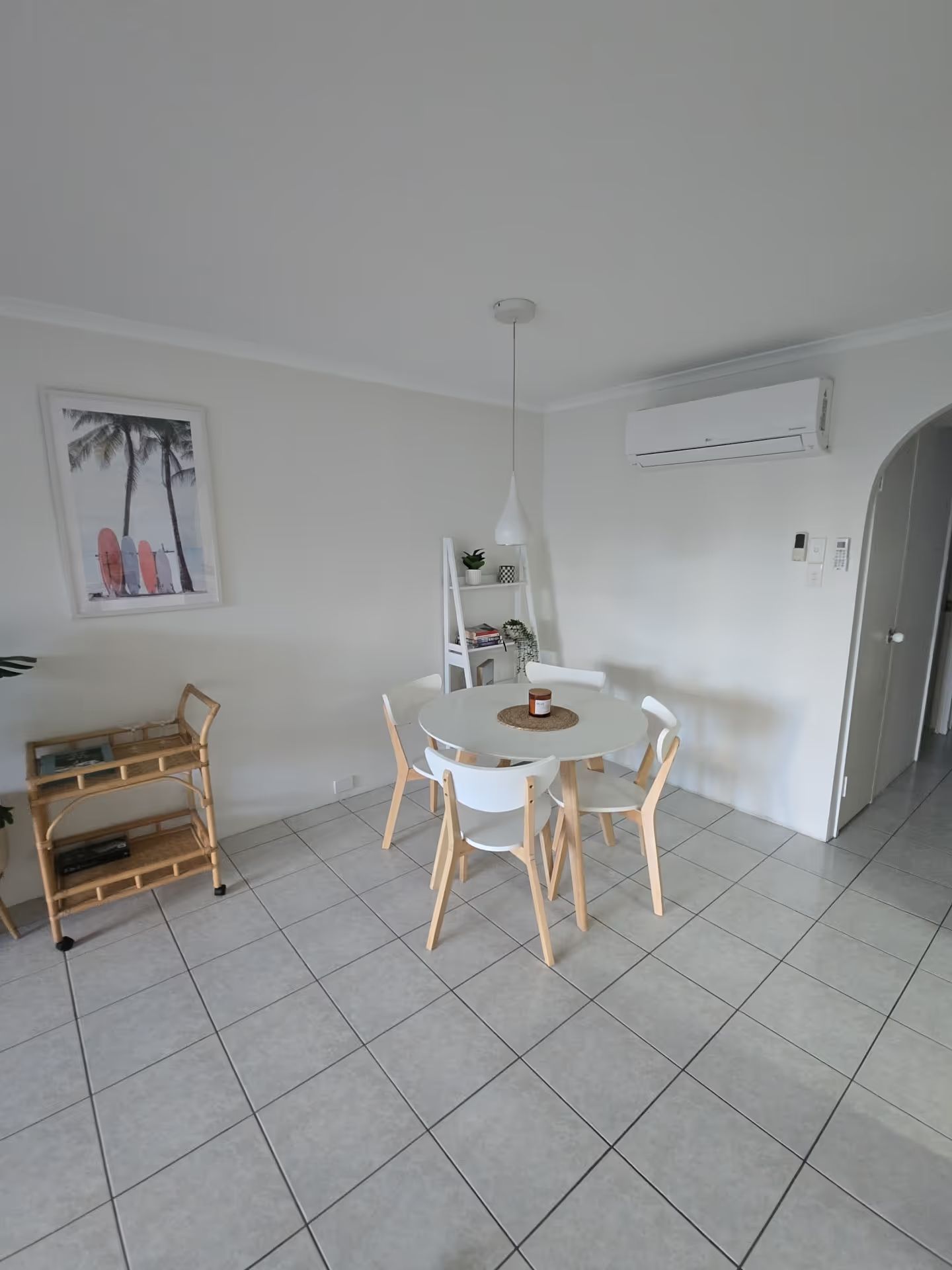 Bright dining room with white table, four wooden chairs, wall art, air conditioner, and tiled floor. Clean airbnb apartment in Main Beach