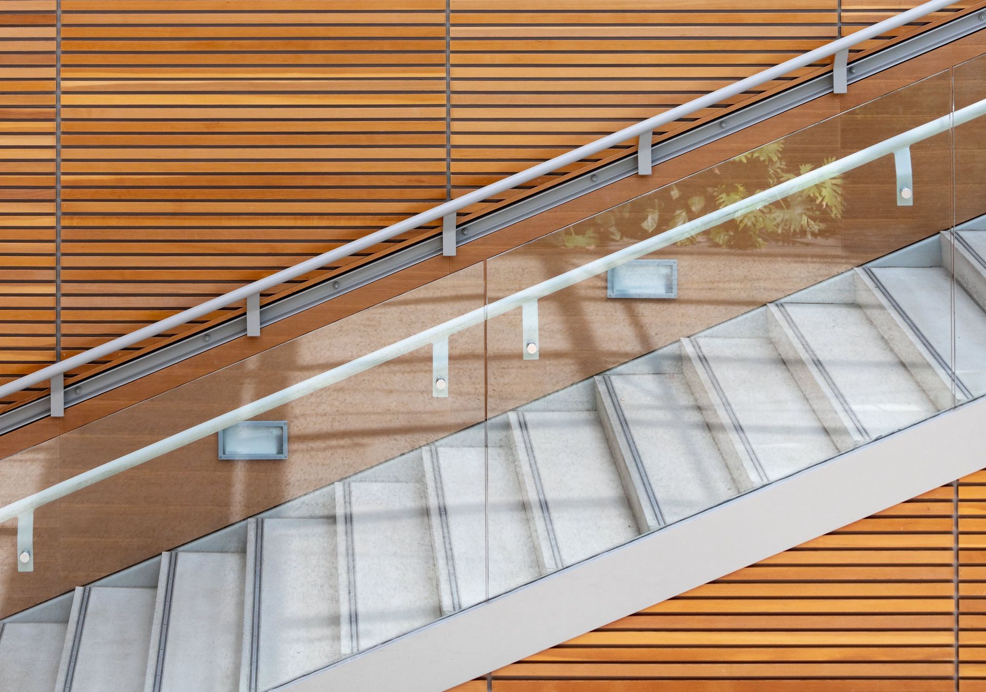 Modern staircase with metal railings and white steps against a wood-paneled wall