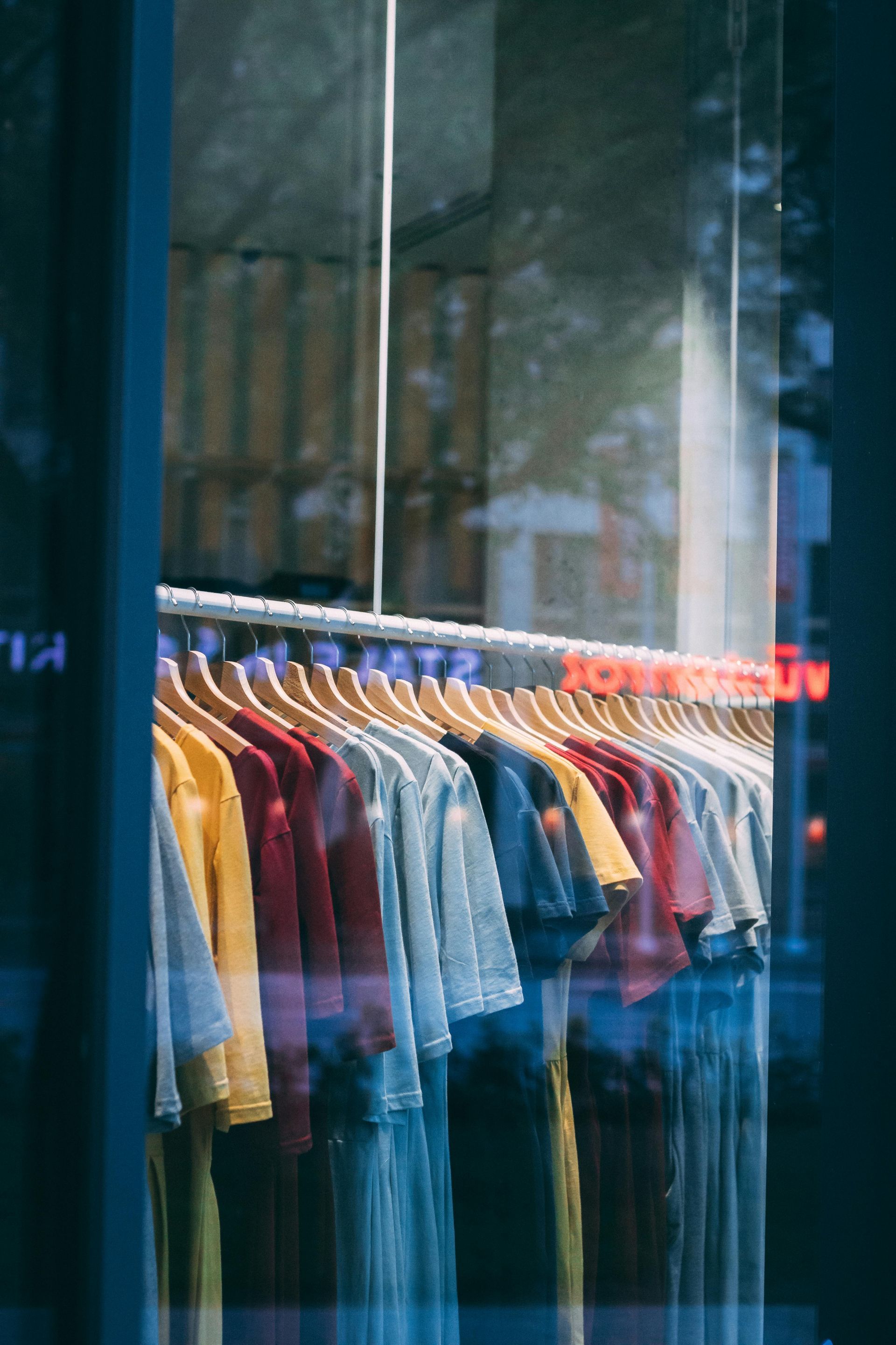 Clothing rack with colorful shirts and jackets displayed behind a shop window