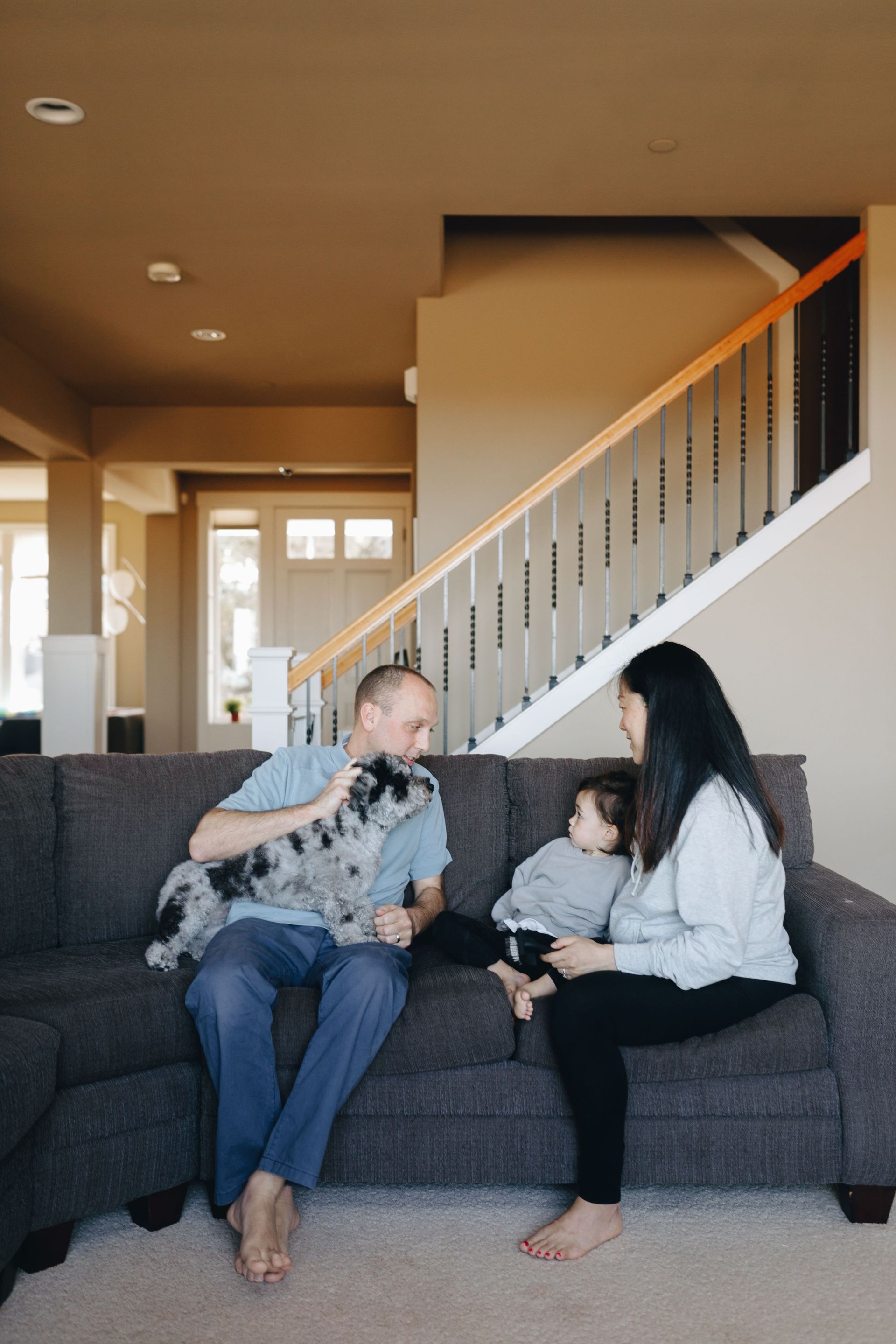 Family and pets in a sunlit living room with a couch, dog on rug, and cat on the sofa