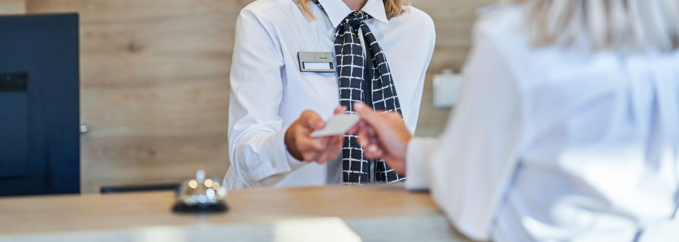 Hotel receptionist handing a card to a guest over the counter.