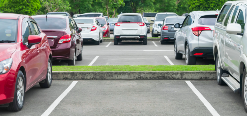 A parking lot with several cars parked in marked spaces, some with visible taillights.