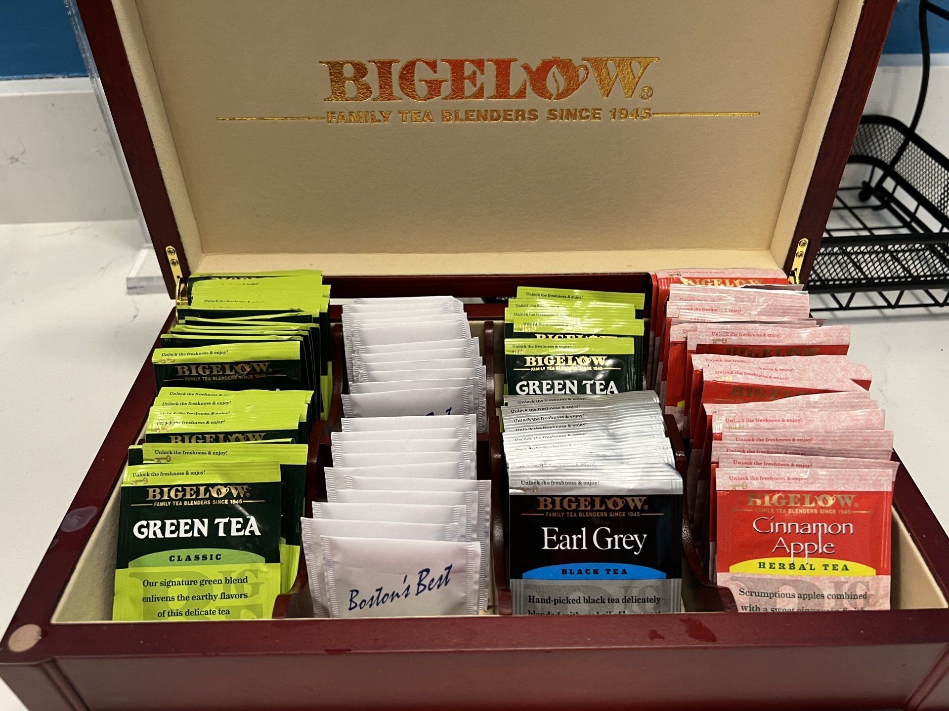 Open wooden tea box filled with Bigelow tea bags: green tea, Earl Grey, and herbal varieties.
