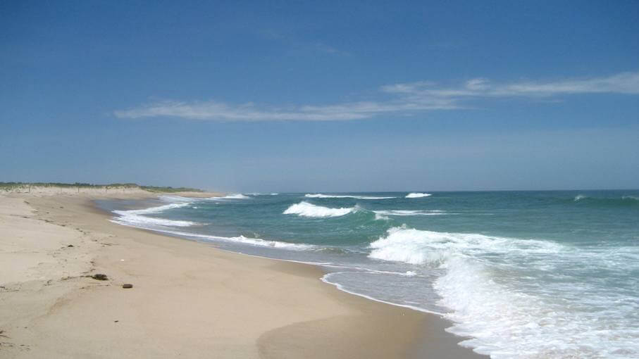 Sandy beach with ocean waves under a blue sky.
