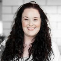 Smiling woman with long dark hair against a light brick wall for mortgage lending