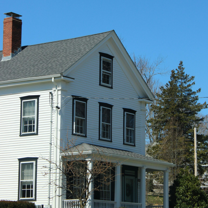 White two-story house with black shutters, a brick chimney, and a porch under a clear blue sky in idaho falls