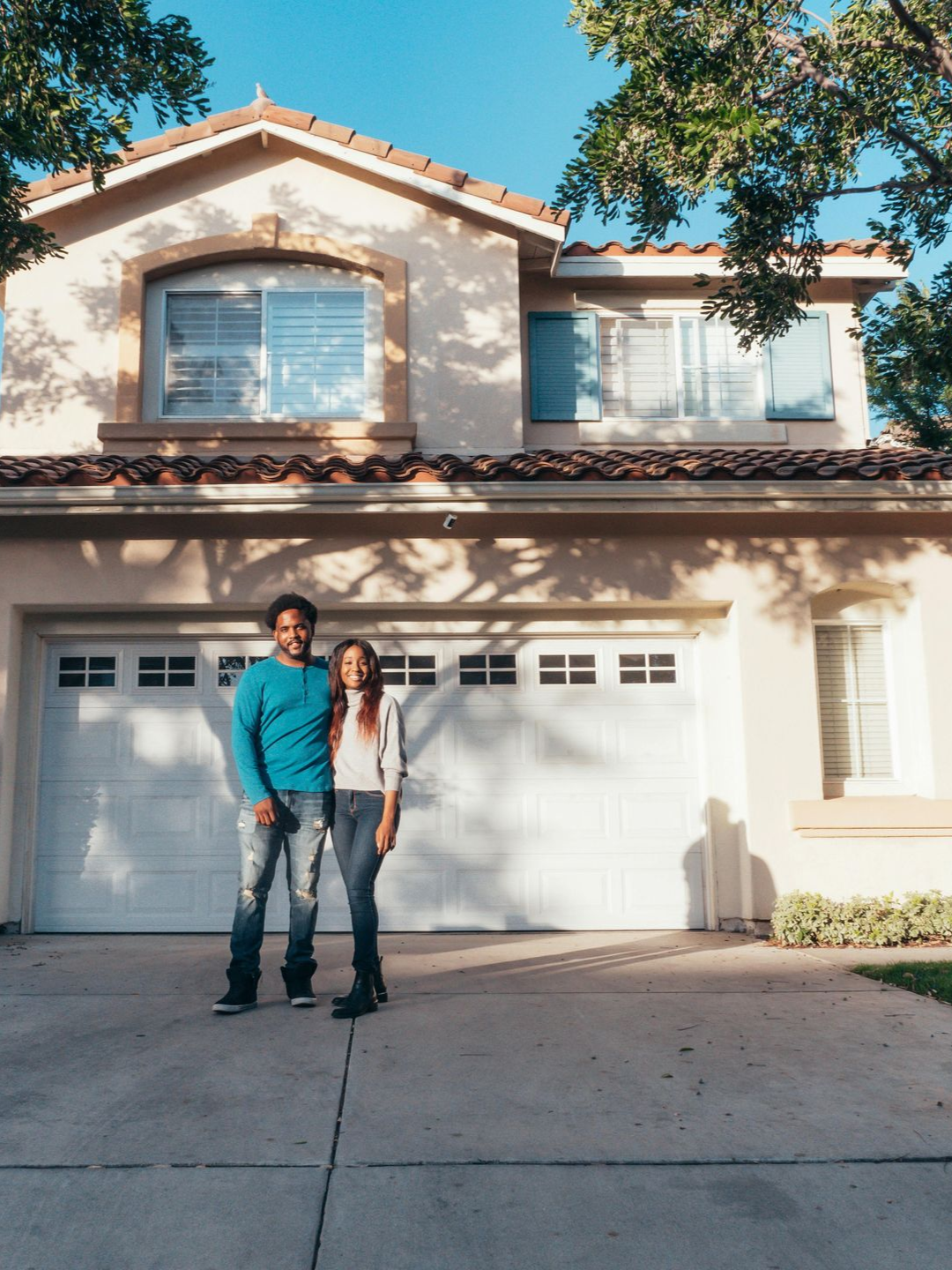 Two people standing in a driveway in front of an idaho falls house with a garage and trees.