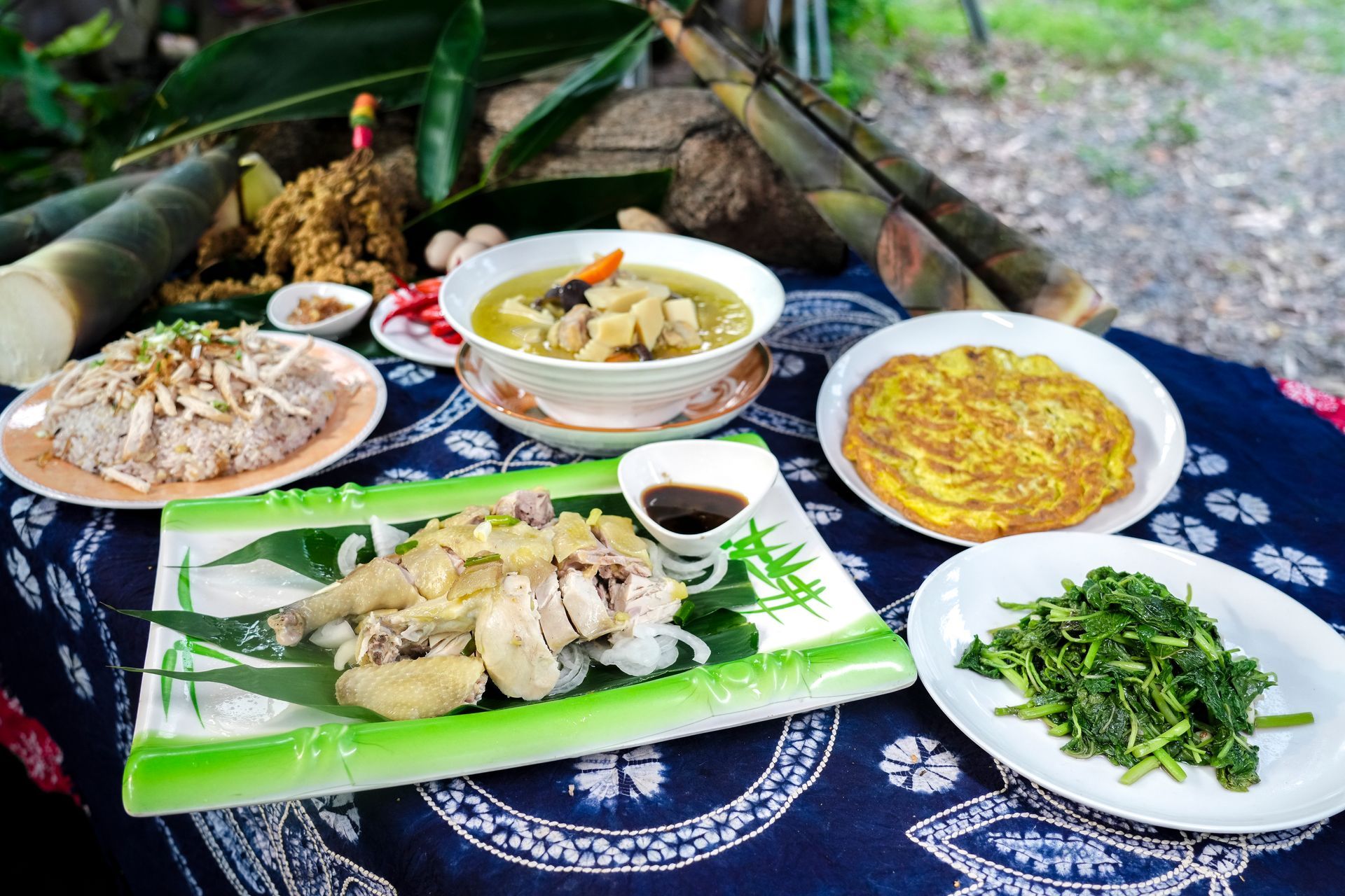 餐桌上的食物:中興紅羽1982土雞肉、雞湯、蛋捲、蔬菜和竹筍,擺放在藍色桌布上。