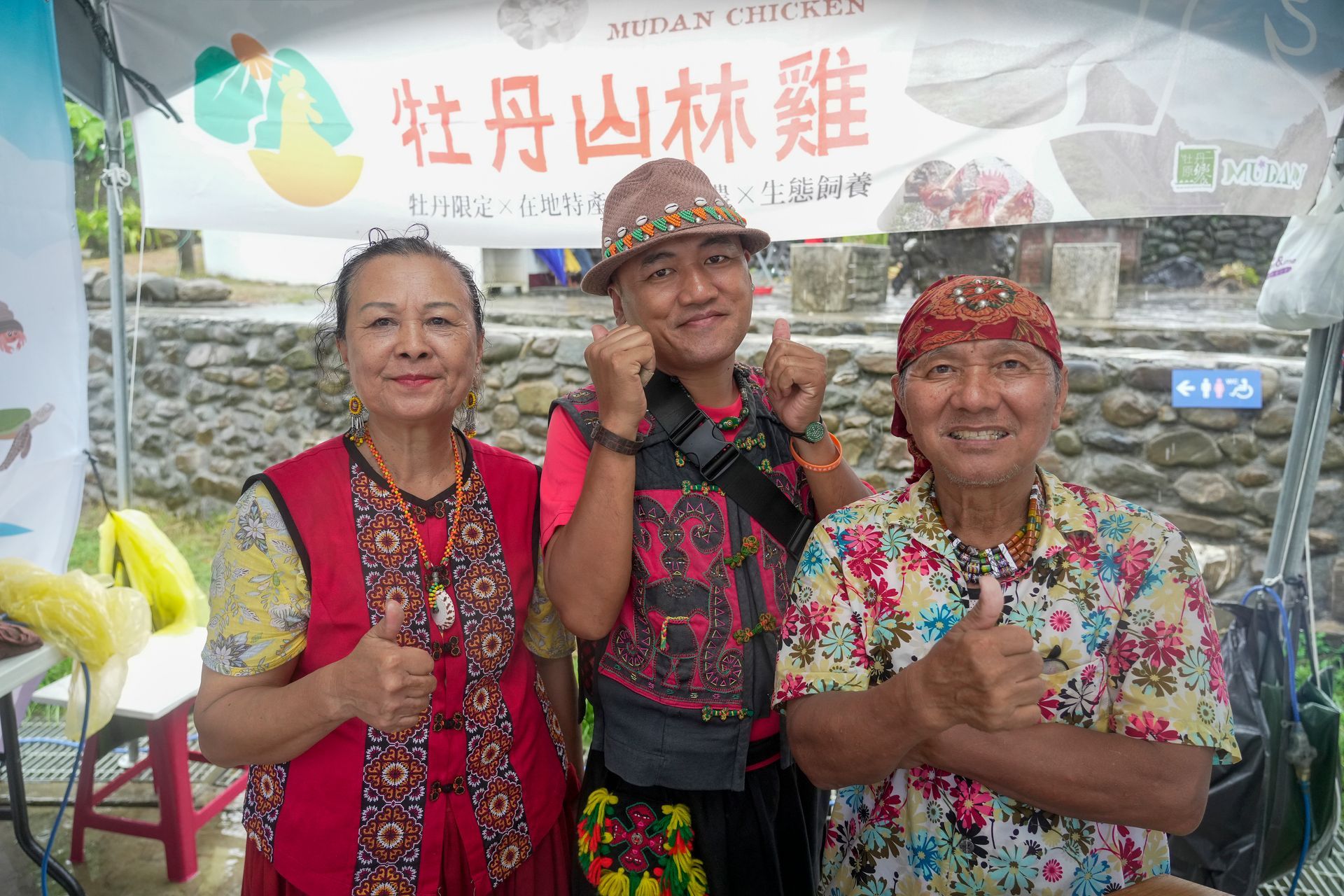 牡丹鄉部落原民三人面帶微笑，豎起大拇指；站在一個標誌前；場景為農夫市集。