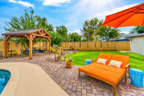 Backyard patio with orange lounge chair, gazebo, pool edge, brick pavers, and wooden fence Backyard patio with orange lounge chair, gazebo, pool edge, brick pavers, and wooden fence