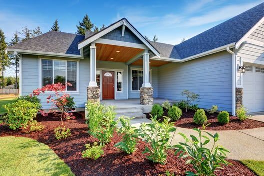 Modern single-story house with a covered front porch, blue siding, and landscaped flower beds.