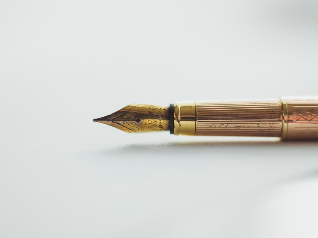 Detailopname van een gouden vulpenpunt op een lichtgrijze achtergrond.