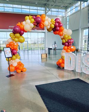 Balloon arch in a bright lobby with white marquee letters and a black floor mat