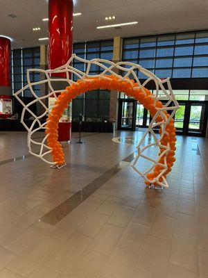 Orange arch sculpture in a modern lobby with a red column and glass windows
