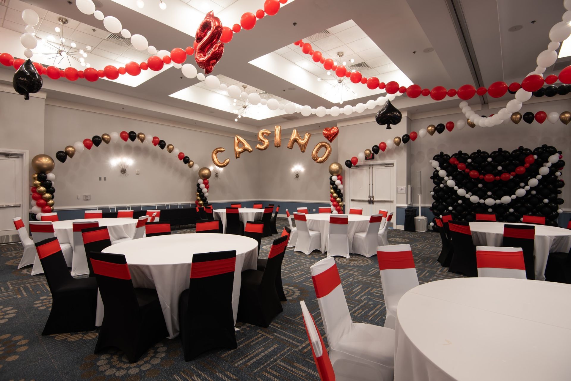 Casino photo area with a red, black, white and gold string-of-pearls balloon arch and gold CASINO lettering.