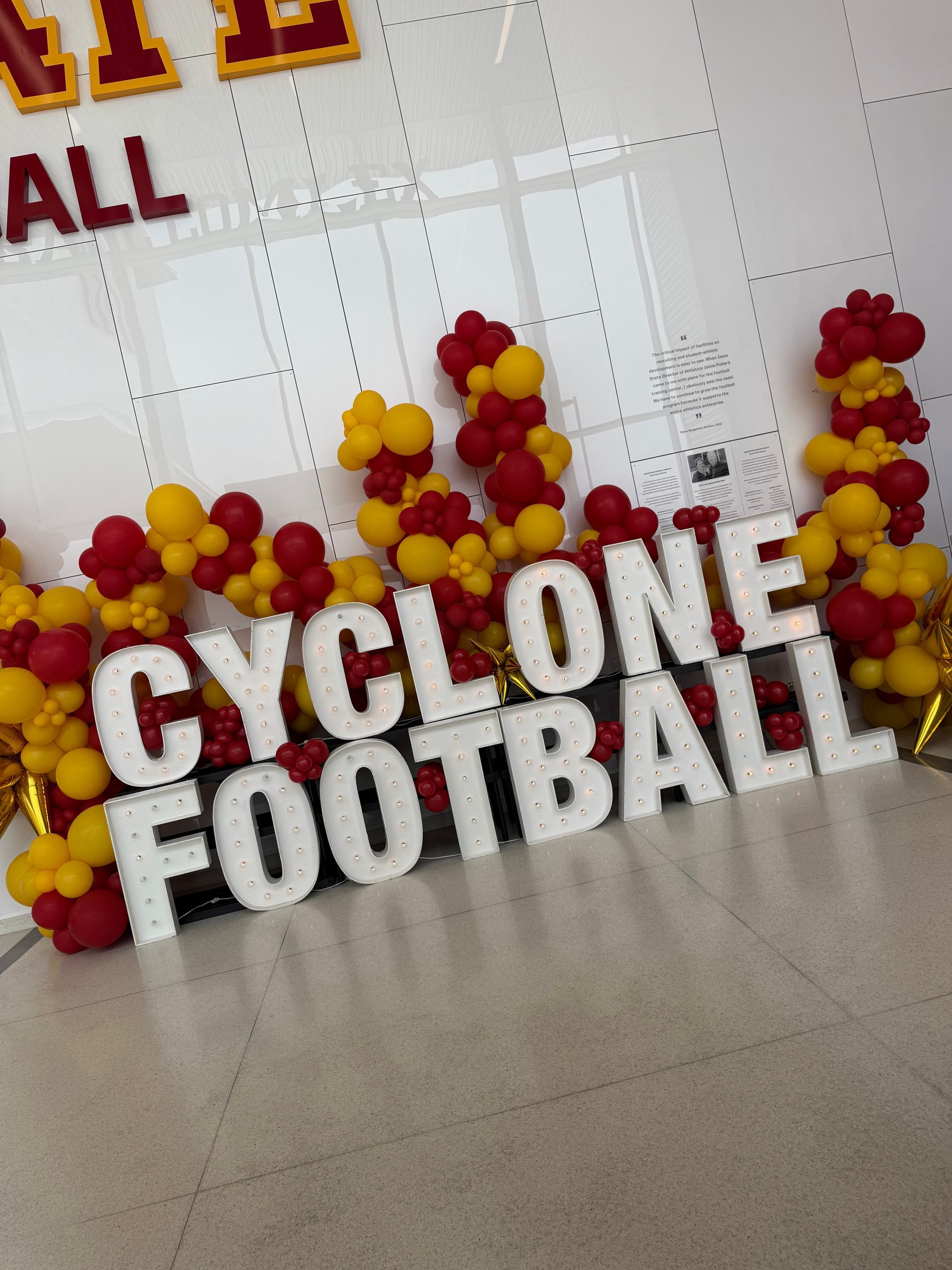 Cardinal and gold balloon décor with illuminated CYCLONE FOOTBALL marquee letters in an indoor hallway.