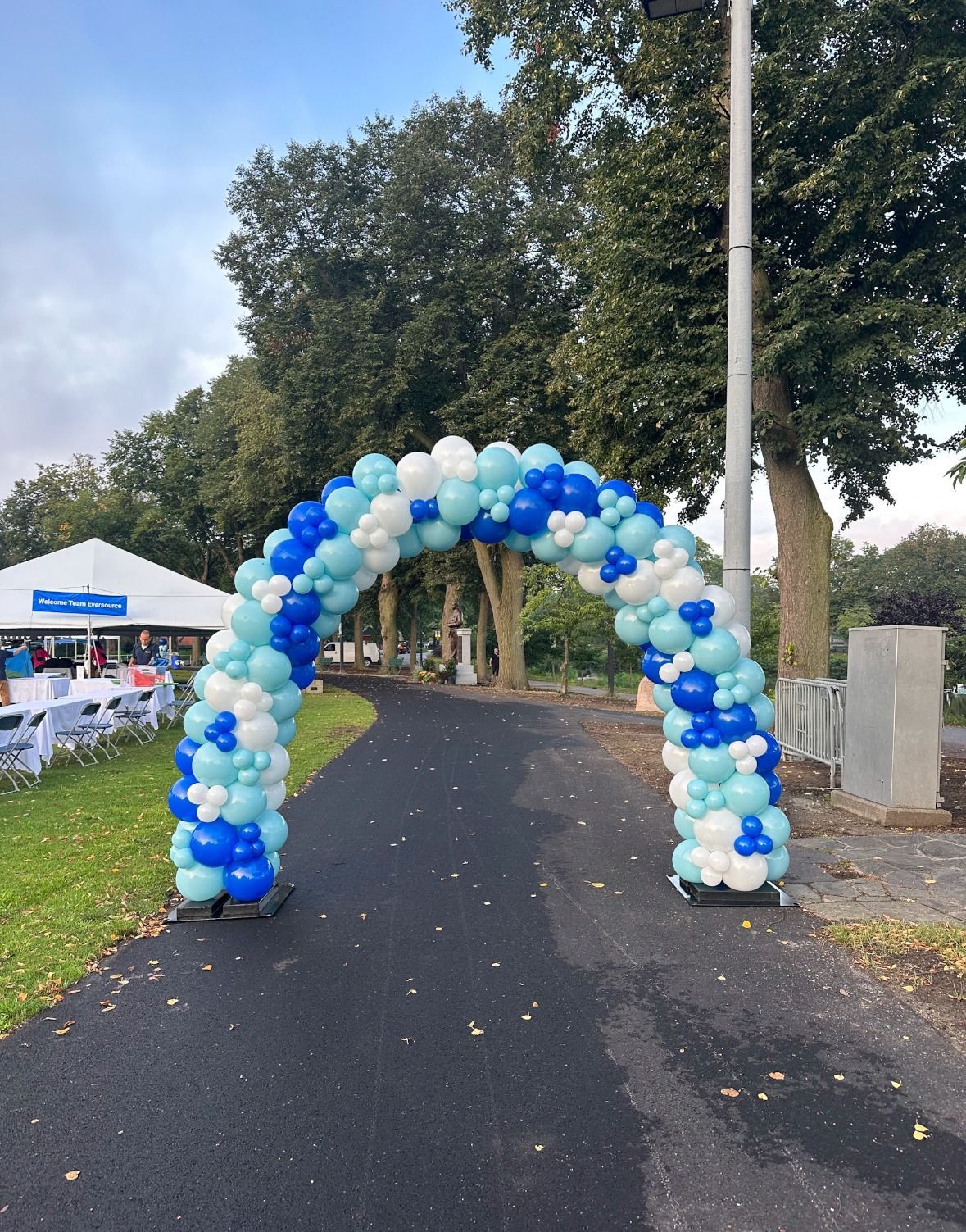Blue, white, and green organic balloon arch over an outdoor pathway