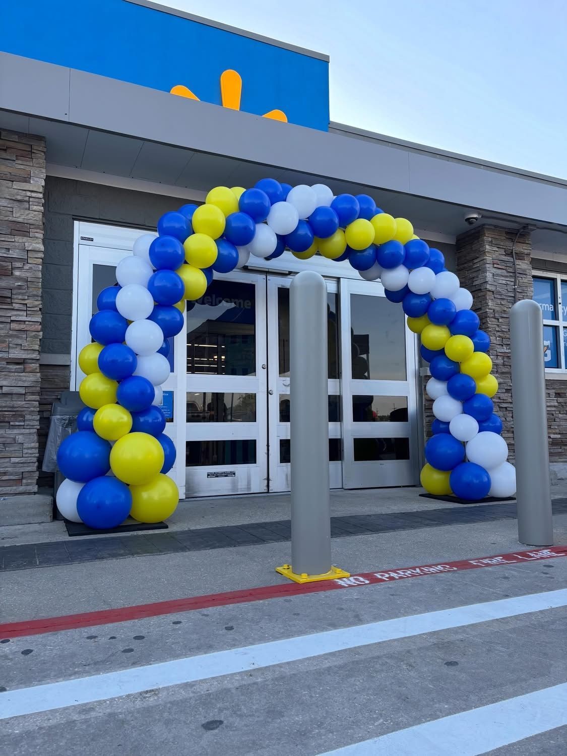 Blue, white, and yellow balloon arch framing exterior double doors
