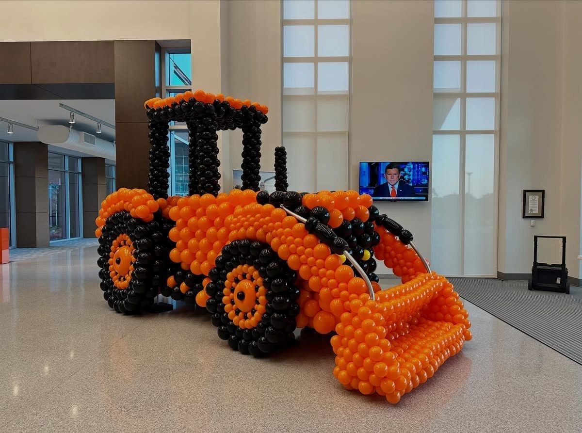 Orange and black construction vehicle balloon sculpture in an indoor lobby
