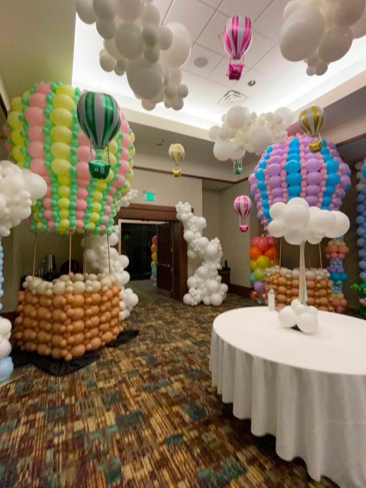 Colorful hot air balloon sculptures above round tables in an event hall