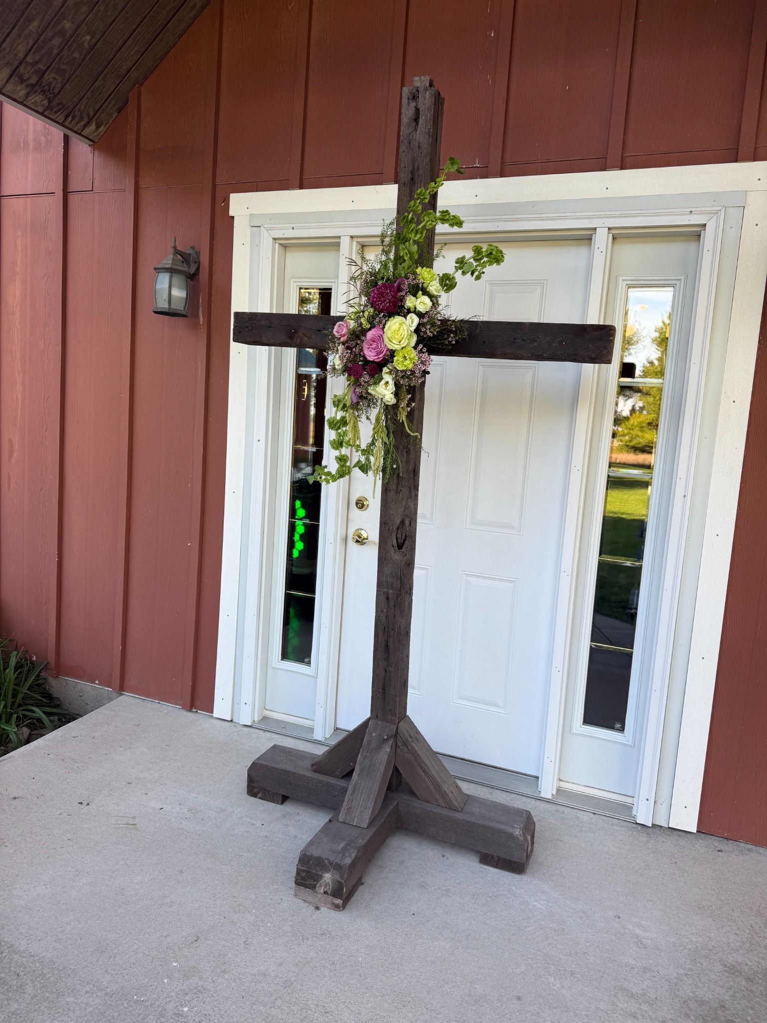 Rustic freestanding wooden cross shown with a floral arrangement