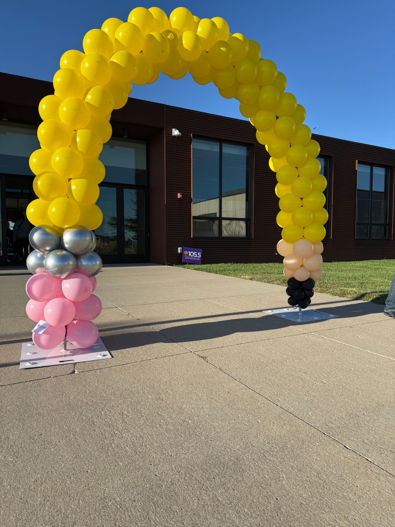 Yellow balloon arch with silver and pink accents outside a storefront