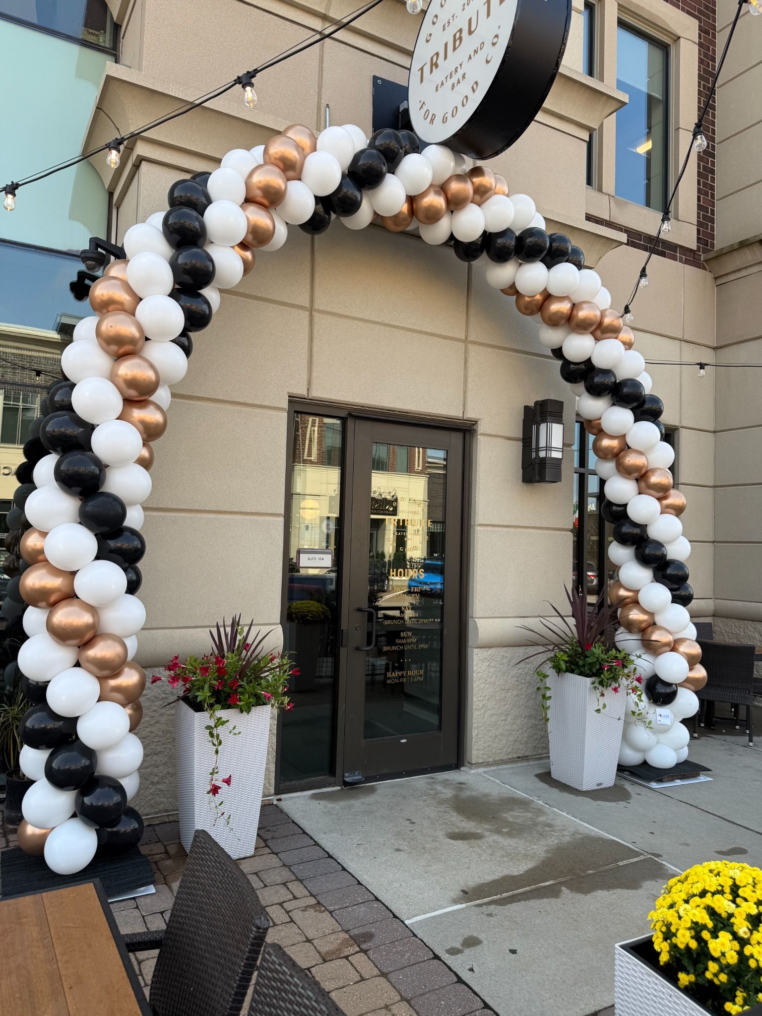 White, black, and champagne balloon arch outside a business entrance