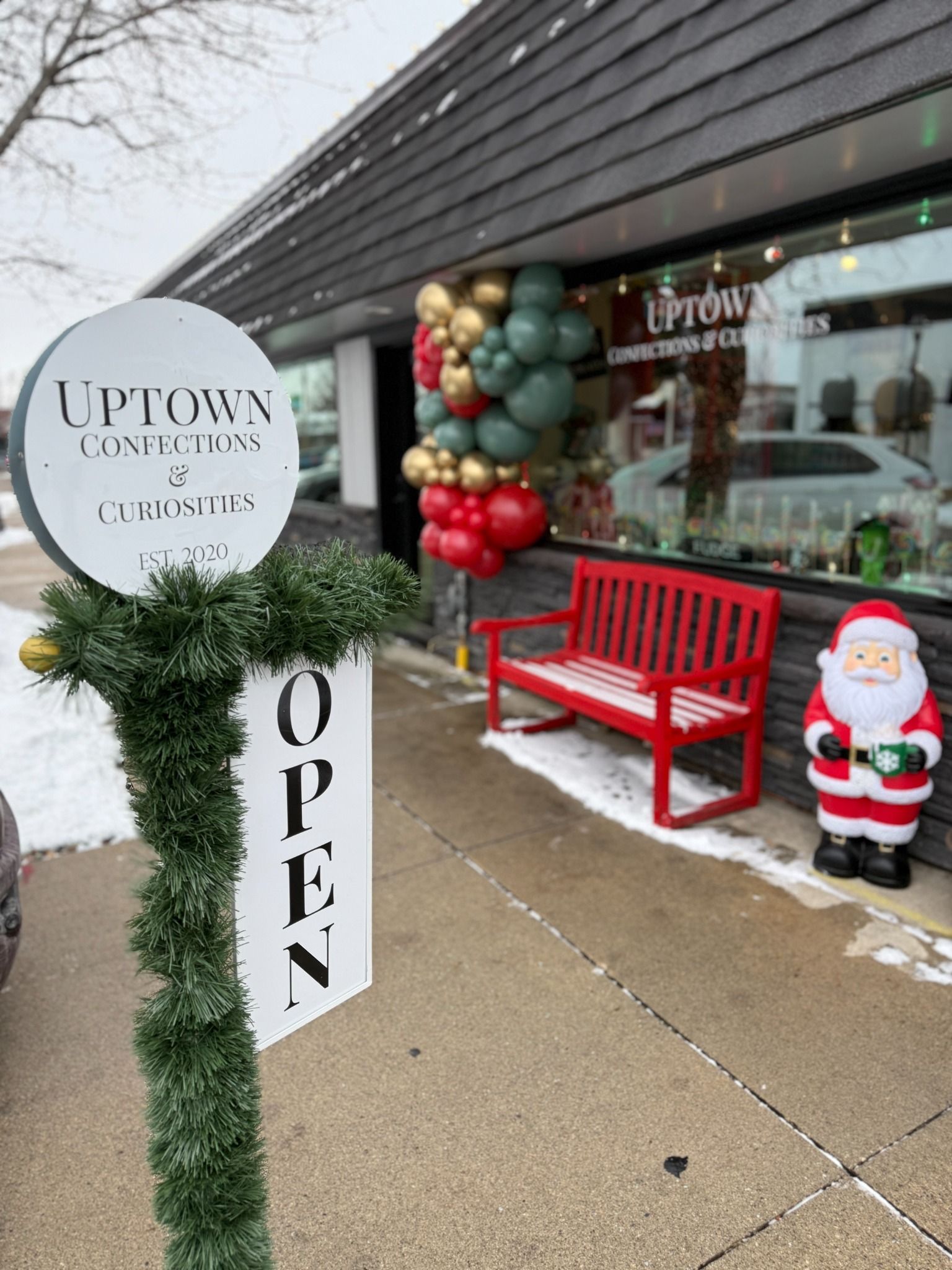 Christmas storefront with holiday balloons, a red bench, and a Santa figure
