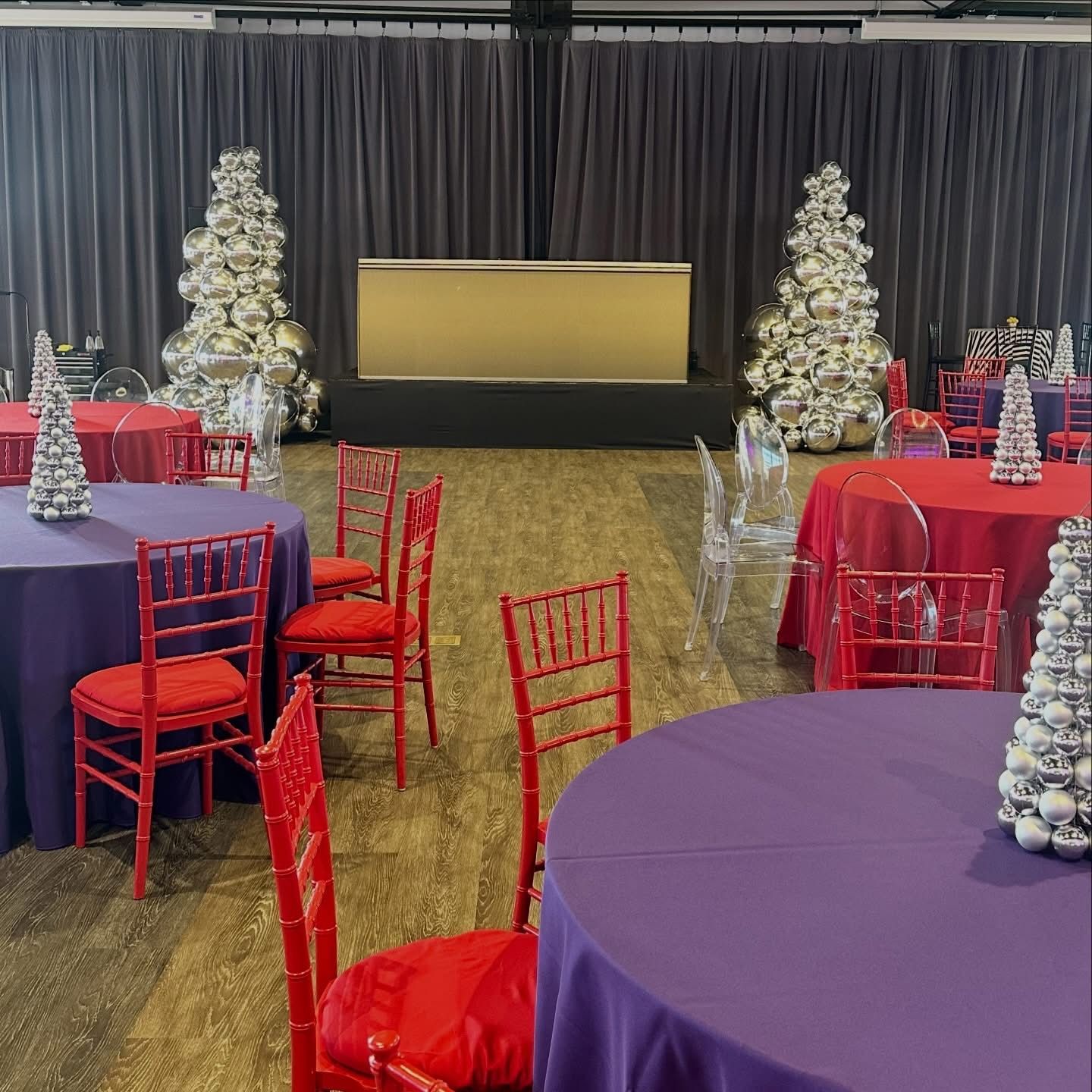 Holiday event room with red chairs, colorful tables, and illuminated Christmas trees