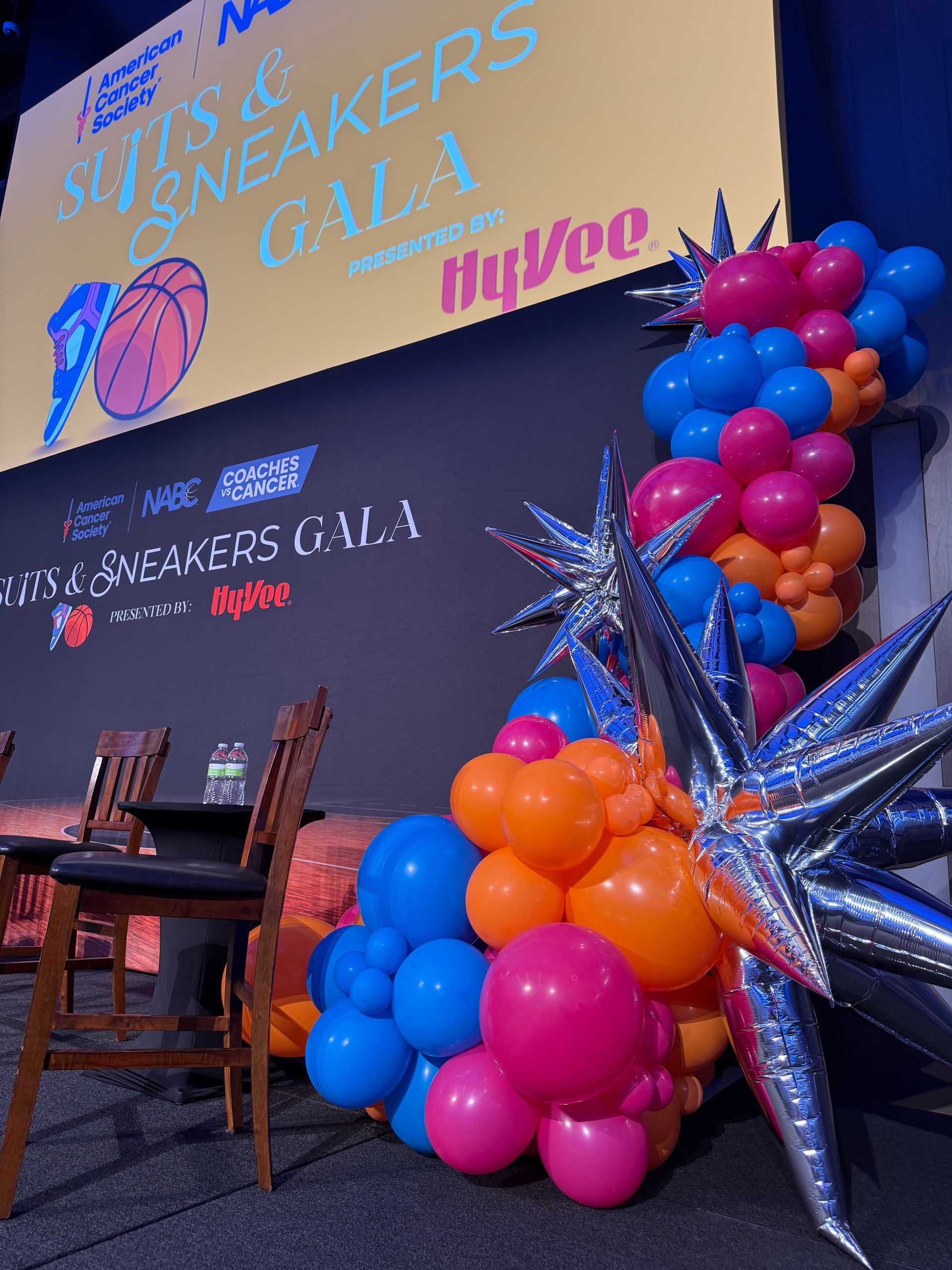 Colorful balloon columns and metallic starburst accents framing the Suits and Sneakers gala stage