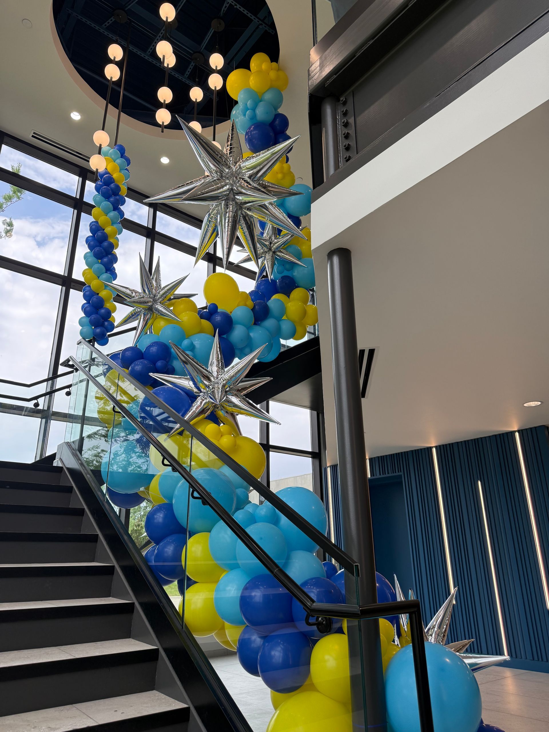 Blue, yellow, and silver balloon installation along an atrium staircase for an Excell Brands company celebration
