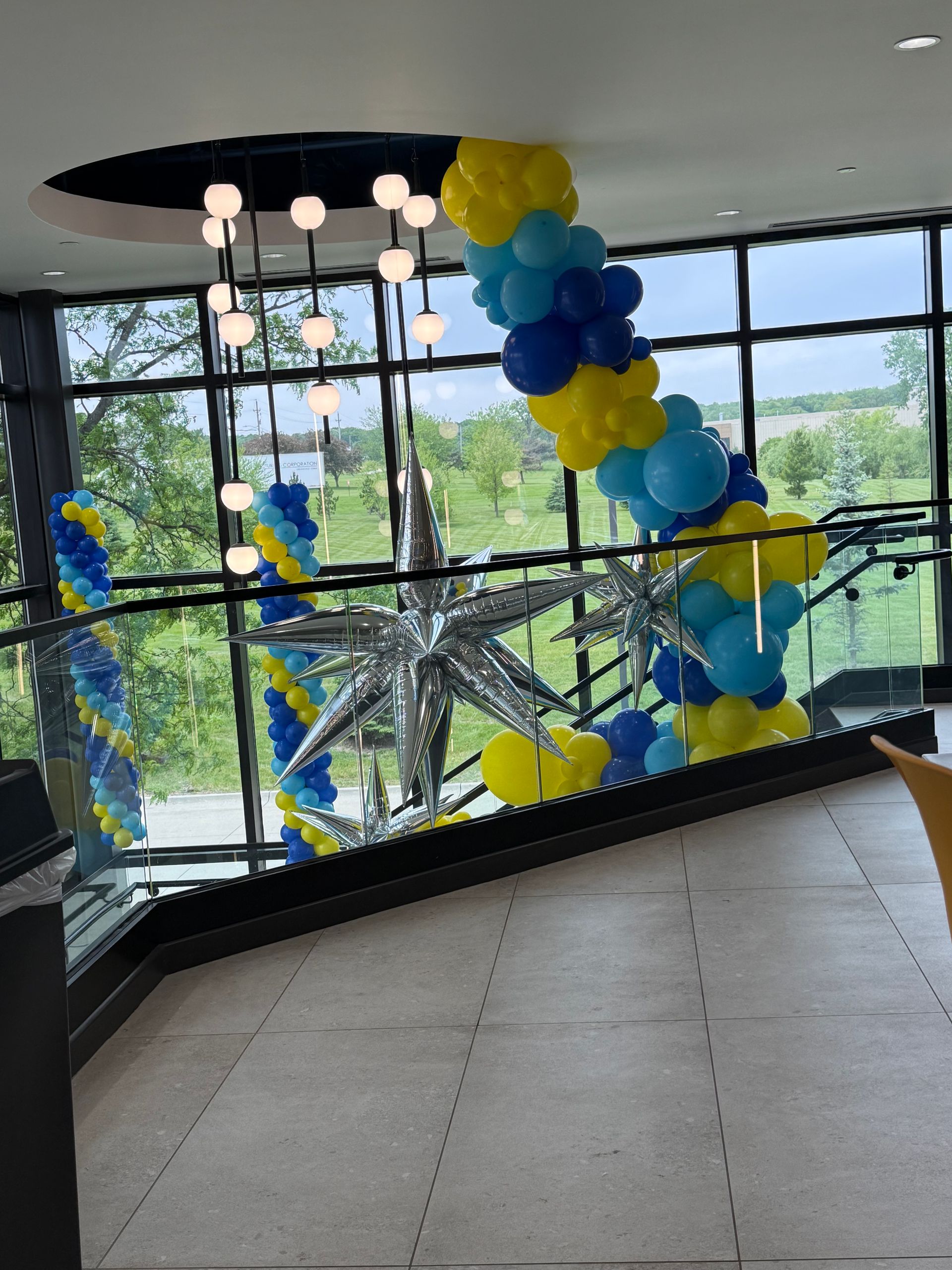 Balloon star sculpture in a bright lobby, decorated with blue and yellow balloons by large windows.