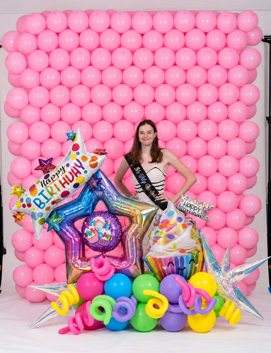 Colorful birthday balloon marquee with stars and cupcake against a pink balloon wall