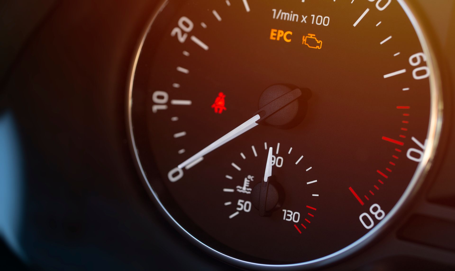 A close up of a car 's speedometer with a red light on it.