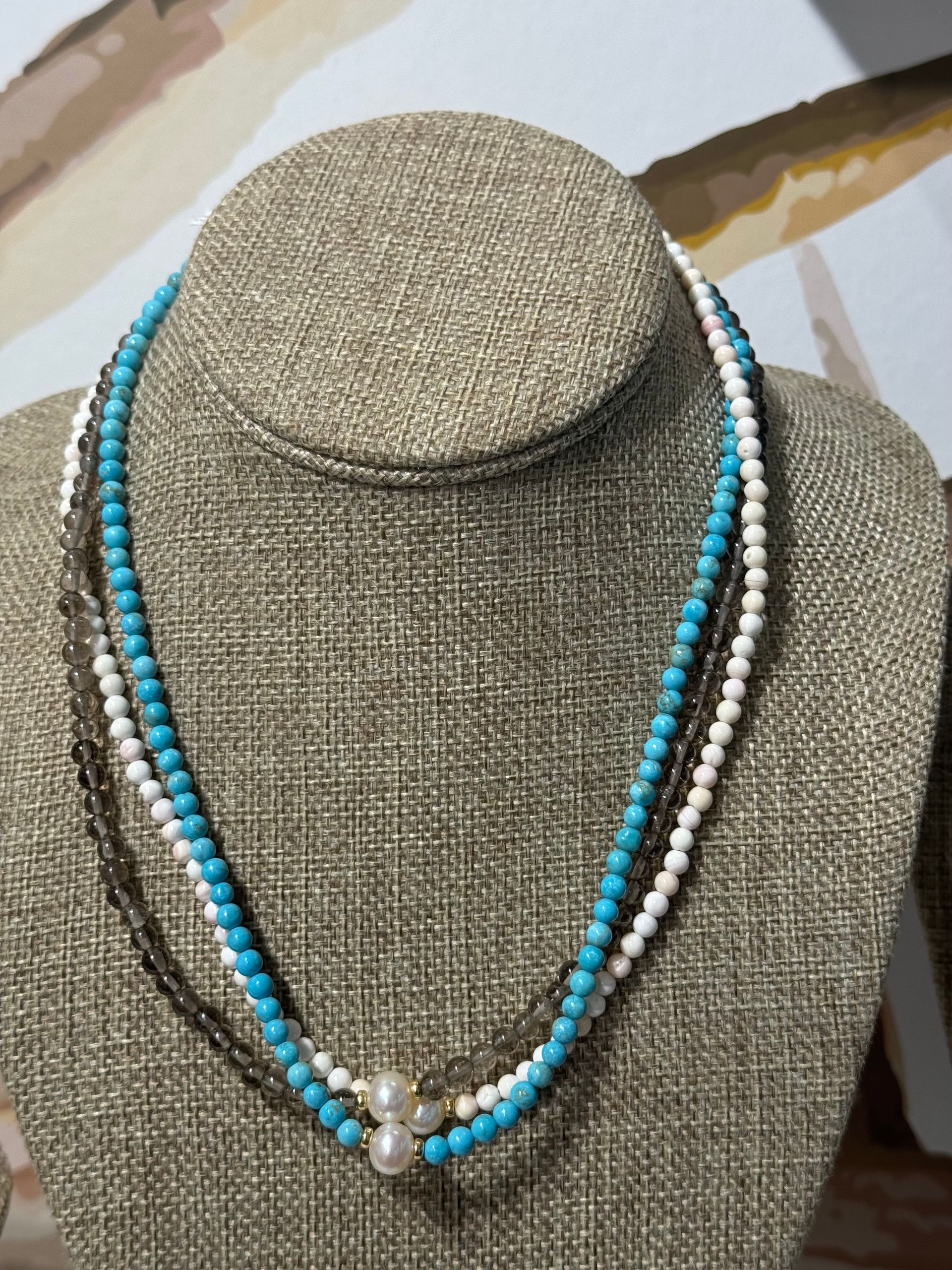 A necklace with turquoise and white beads is on a mannequin