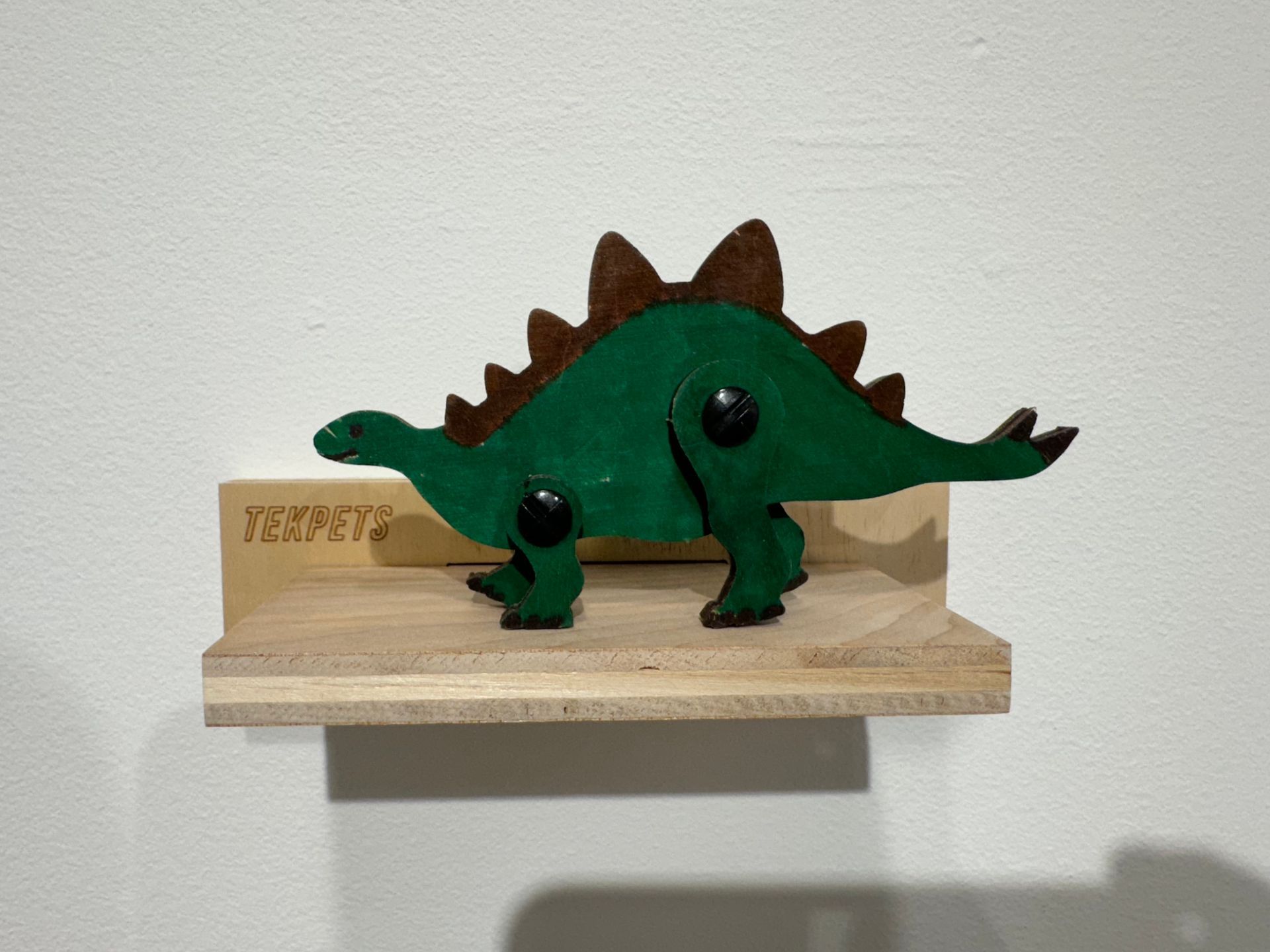 A wooden shelf with a green dinosaur on it