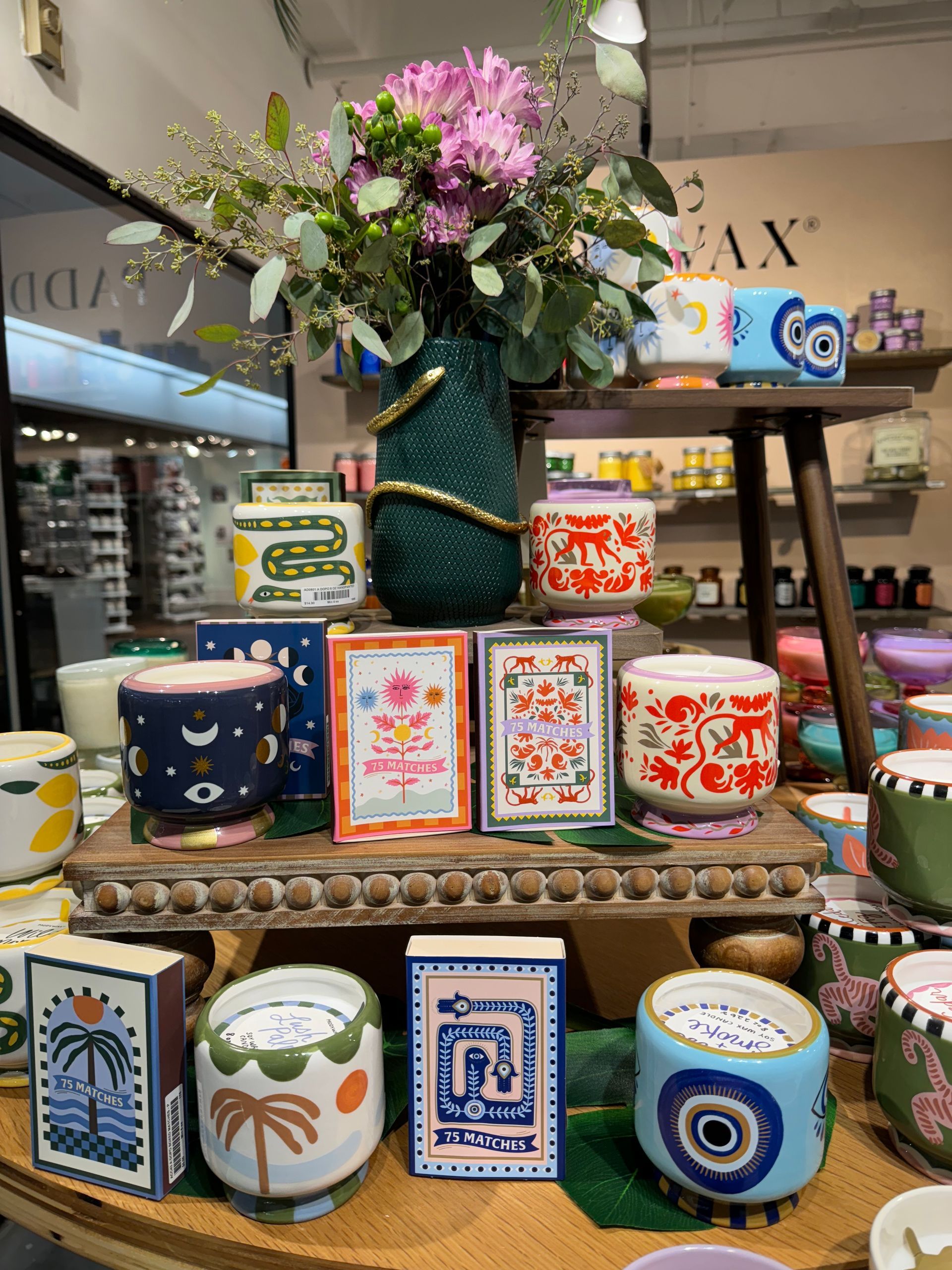 A display of candles with a vase of flowers in the background