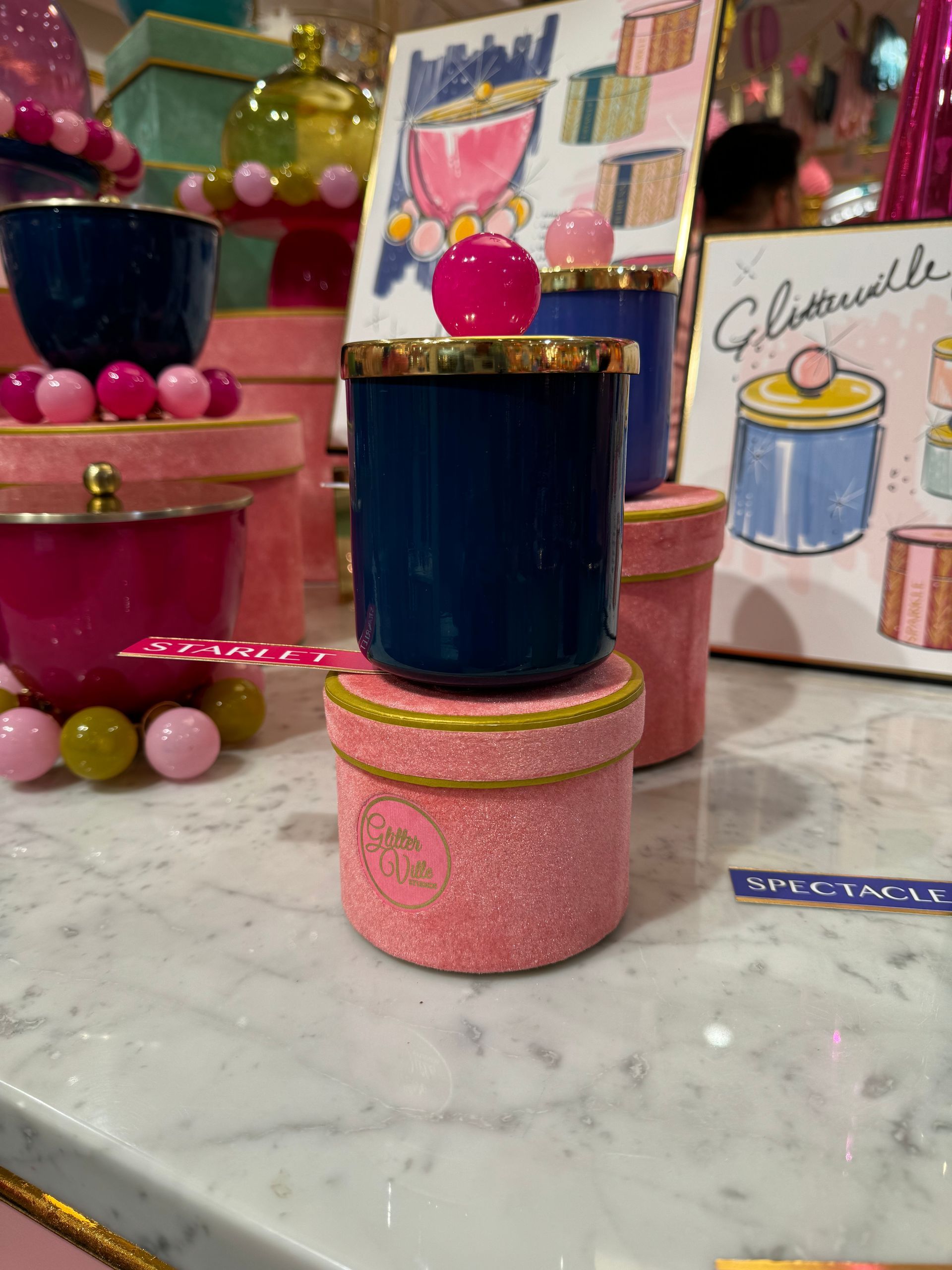 A candle in a pink box with a pink cherry on top