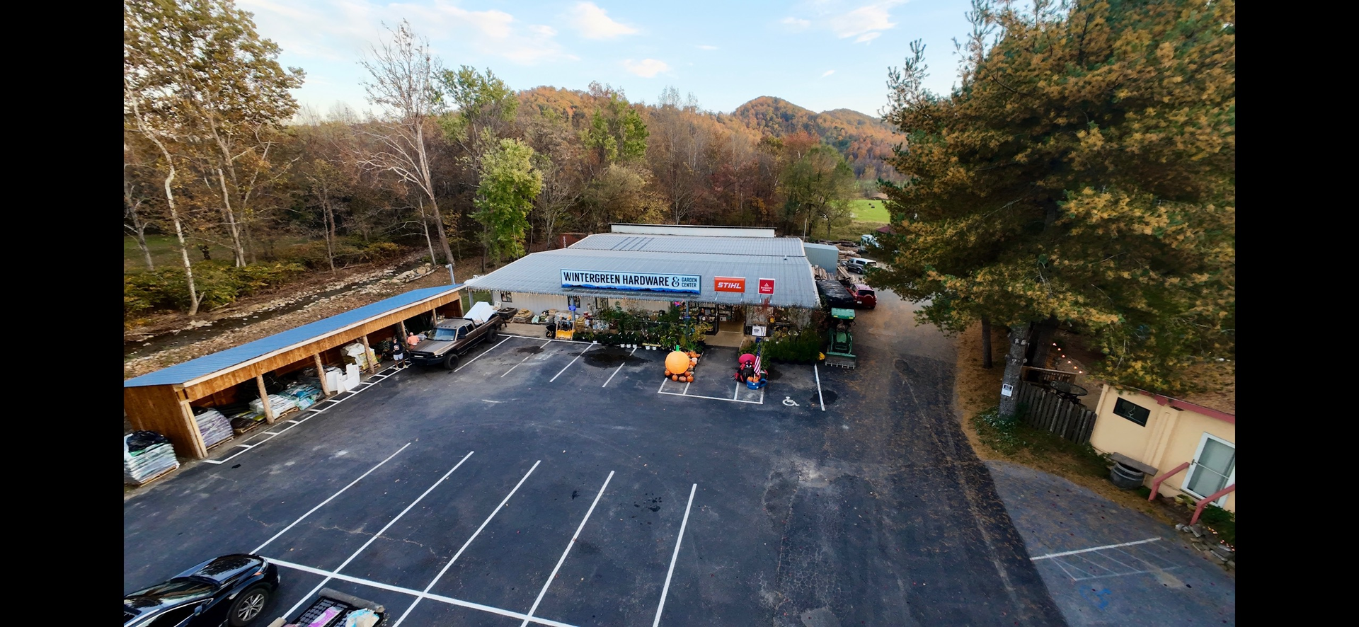 Exterior view of a roadside shop with parking lot and surrounding trees under a blue sky.