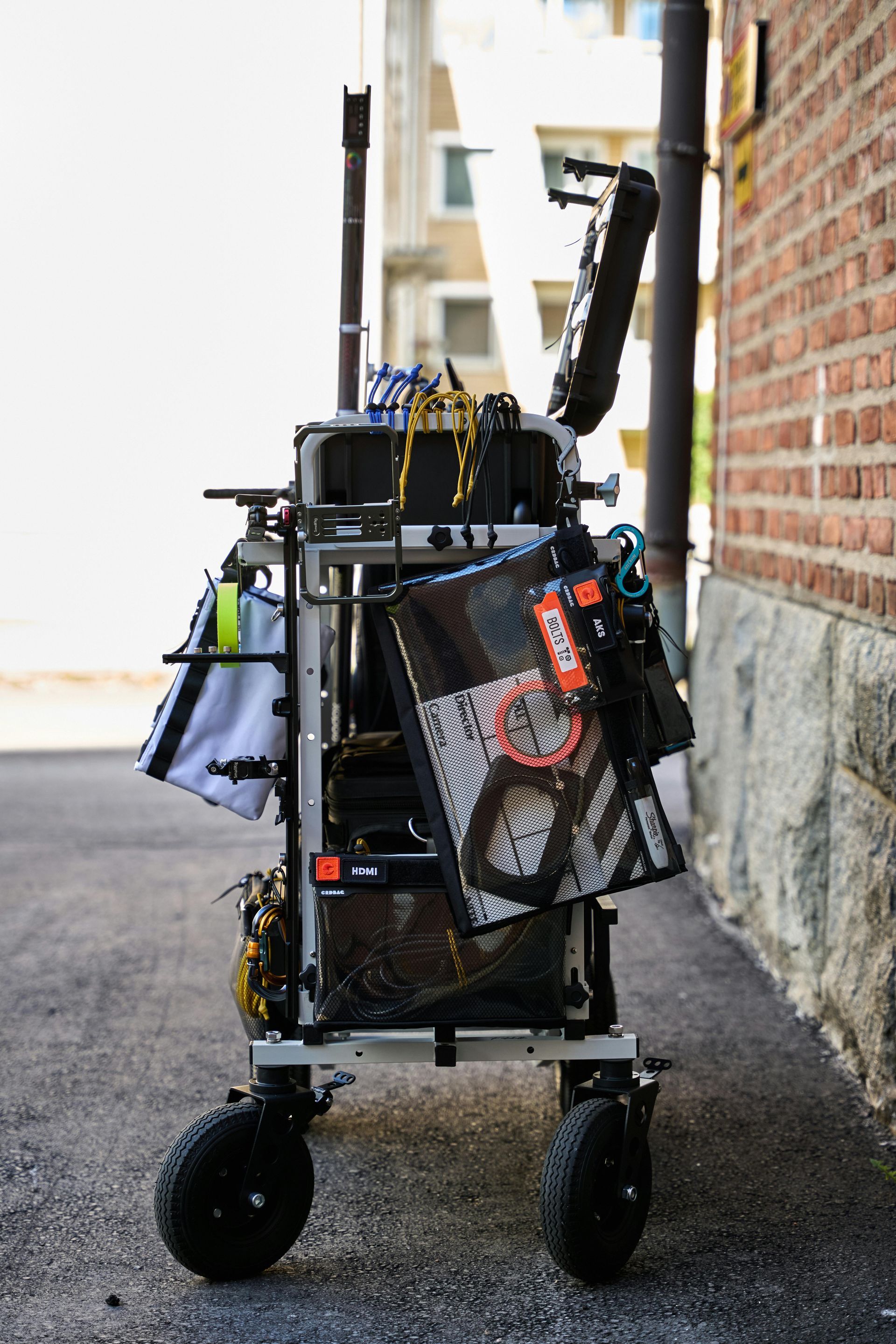 A production cart loaded with equipment, parked in an alleyway next to a brick wall.